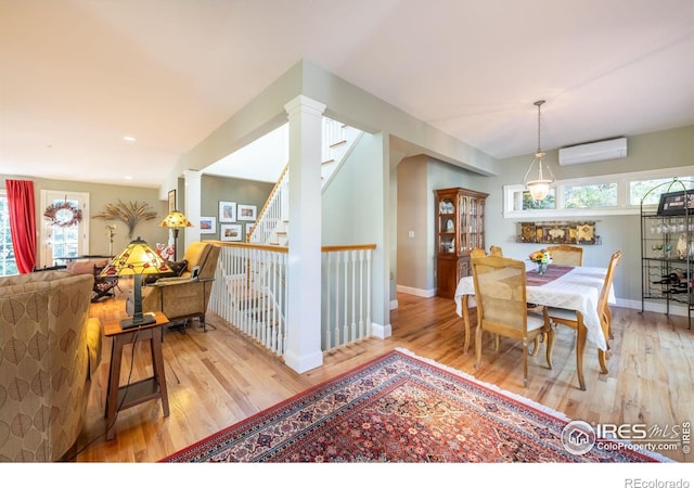 dining room with ornate columns, a wealth of natural light, a wall unit AC, and light hardwood / wood-style flooring