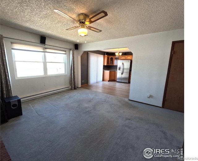 unfurnished living room featuring baseboard heating, ceiling fan, and a textured ceiling