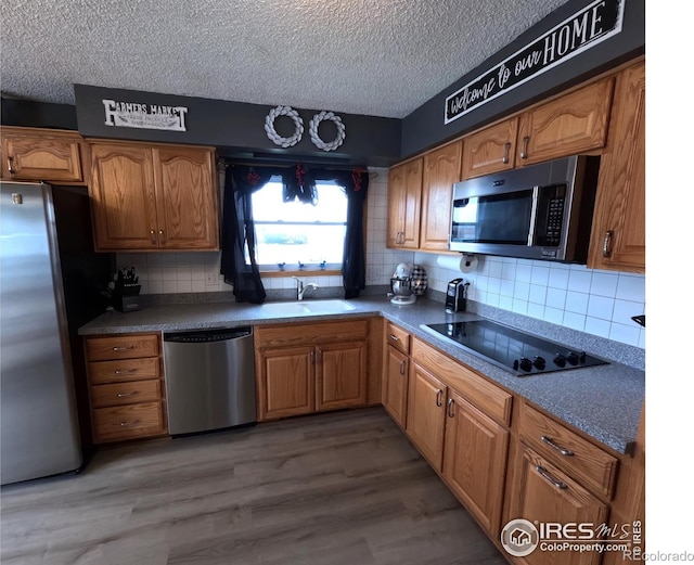 kitchen featuring wood-type flooring, sink, backsplash, stainless steel appliances, and a textured ceiling