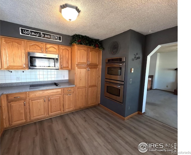 kitchen with appliances with stainless steel finishes, a textured ceiling, backsplash, and dark hardwood / wood-style flooring