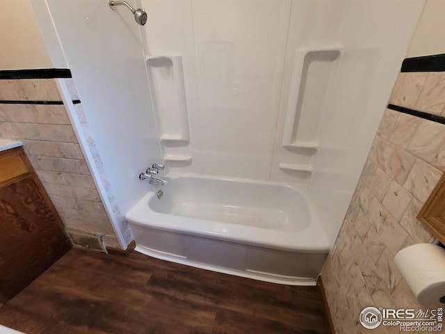 bathroom with tile walls, wood-type flooring, vanity, and shower / washtub combination