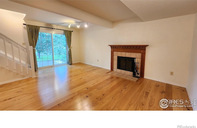 unfurnished living room featuring a tiled fireplace, beamed ceiling, and light wood-type flooring