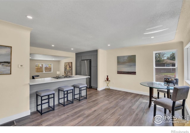 kitchen with stainless steel fridge, a textured ceiling, hardwood / wood-style flooring, and a breakfast bar area