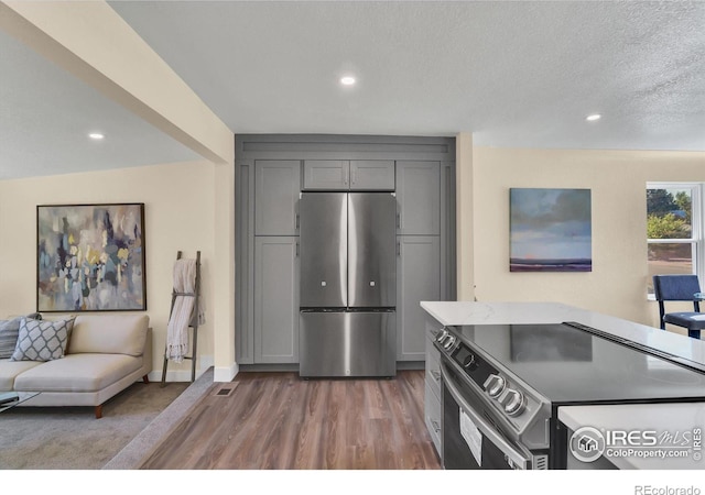 kitchen with a textured ceiling, wood-type flooring, stainless steel appliances, and gray cabinetry