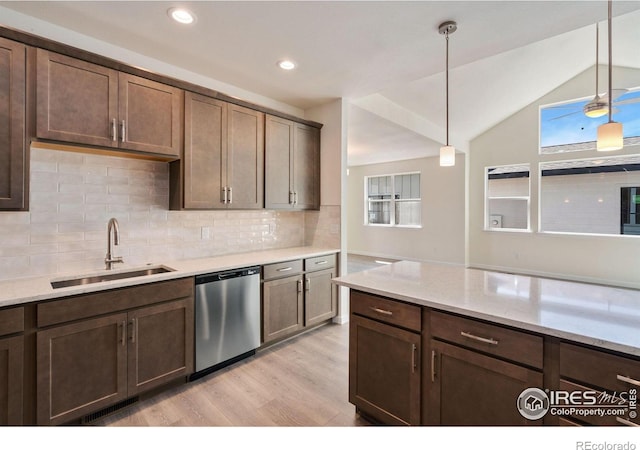 kitchen featuring decorative light fixtures, light wood finished floors, stainless steel dishwasher, vaulted ceiling, and a sink