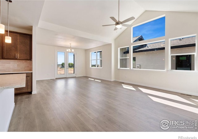 unfurnished living room featuring visible vents, wood finished floors, high vaulted ceiling, baseboards, and ceiling fan with notable chandelier