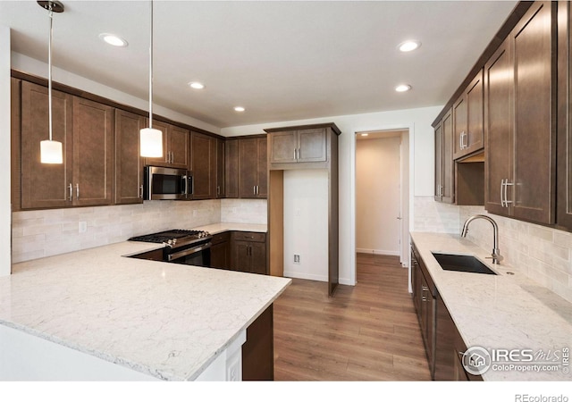 kitchen with stainless steel appliances, light stone countertops, a sink, dark brown cabinets, and wood finished floors