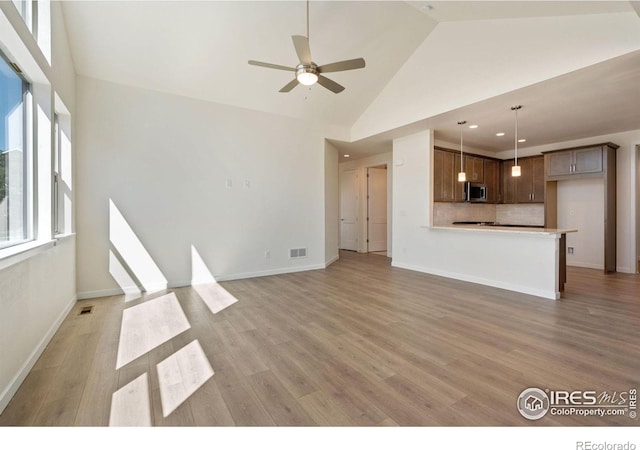 unfurnished living room with ceiling fan, high vaulted ceiling, light wood finished floors, and visible vents