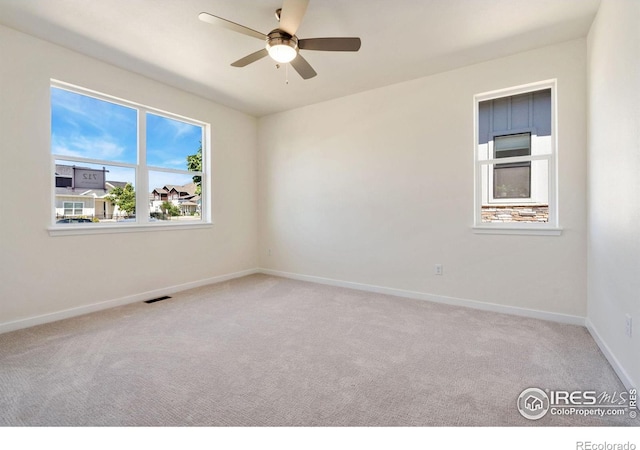 carpeted spare room featuring a ceiling fan, visible vents, and baseboards