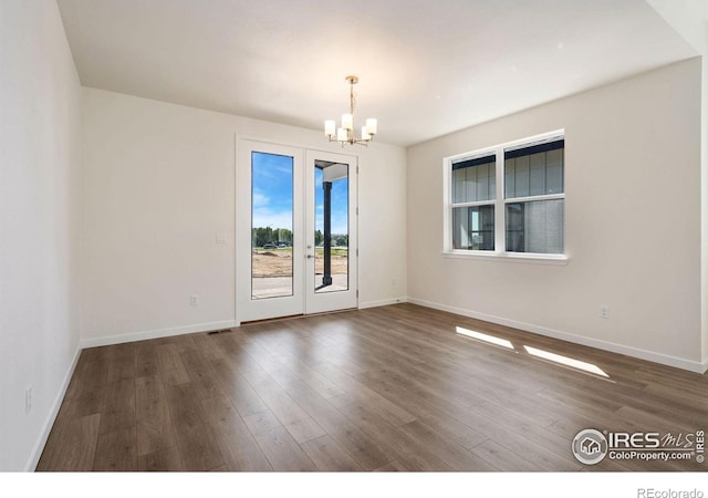 spare room featuring a chandelier, dark wood-style flooring, and baseboards