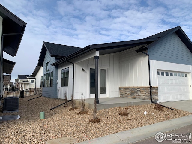 view of front of house featuring concrete driveway, stone siding, an attached garage, cooling unit, and board and batten siding