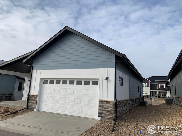 view of front of house with a garage, stone siding, central AC, and driveway