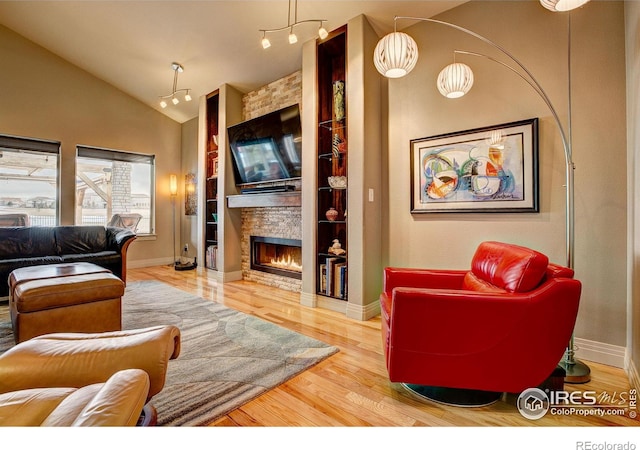 living room featuring vaulted ceiling, hardwood / wood-style floors, and a stone fireplace