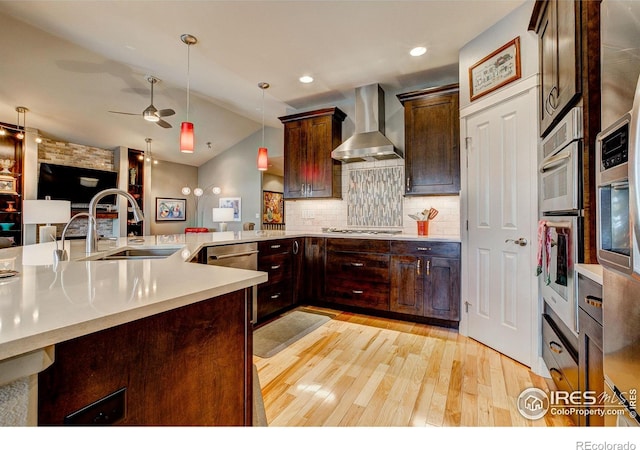 kitchen with vaulted ceiling, light hardwood / wood-style floors, sink, ceiling fan, and wall chimney range hood