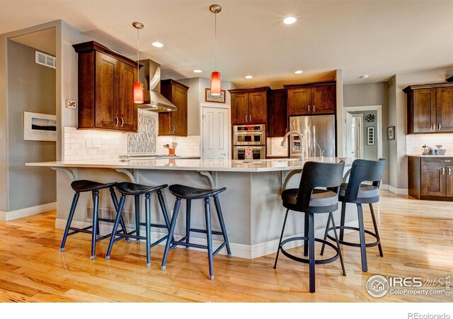 kitchen with wall chimney exhaust hood, light hardwood / wood-style flooring, appliances with stainless steel finishes, and a breakfast bar