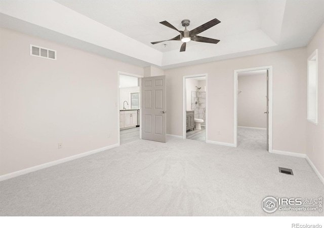 unfurnished bedroom featuring connected bathroom, a closet, ceiling fan, a tray ceiling, and a walk in closet