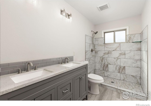 bathroom featuring hardwood / wood-style floors, toilet, tiled shower, vanity, and decorative backsplash