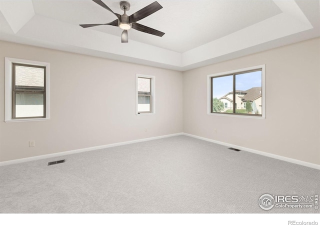 carpeted spare room with ceiling fan and a raised ceiling