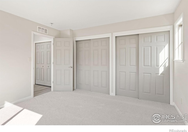 unfurnished bedroom with two closets and light carpet