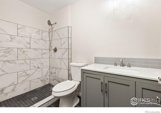 bathroom featuring toilet, a tile shower, backsplash, and vanity