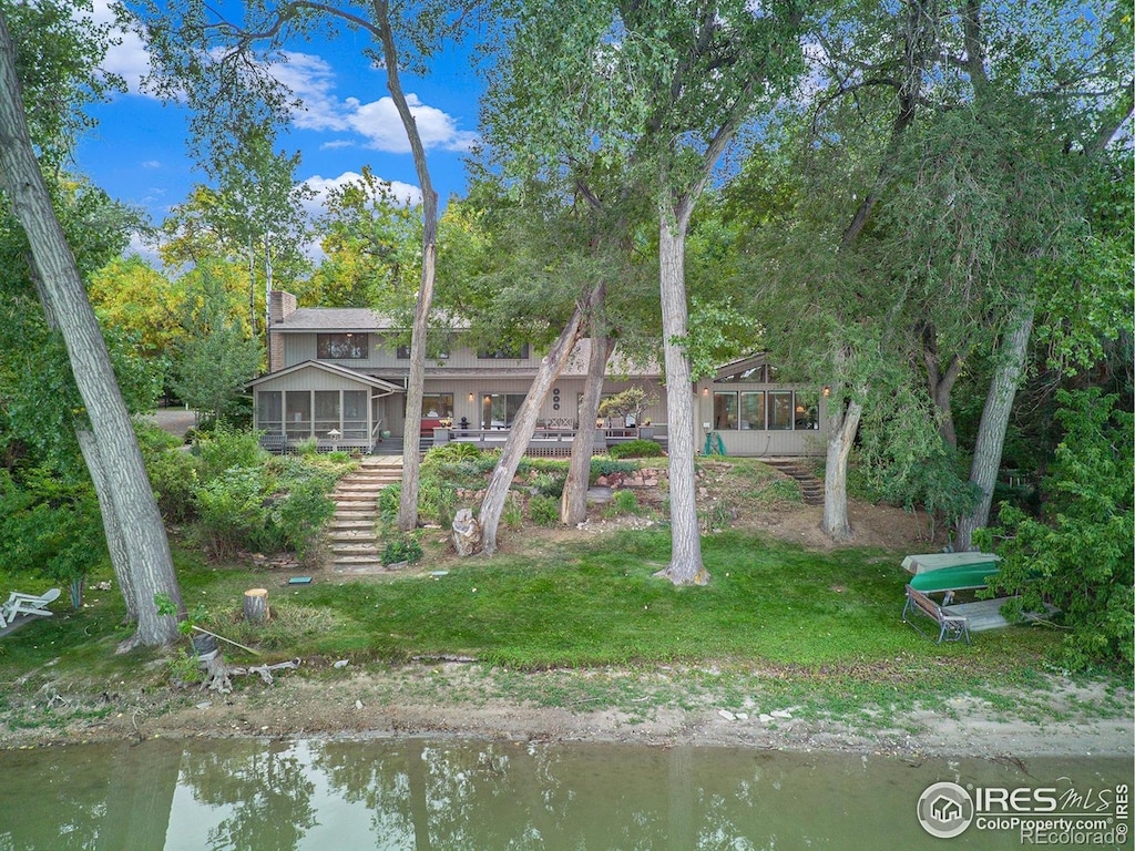 rear view of property featuring a sunroom, a yard, and a water view