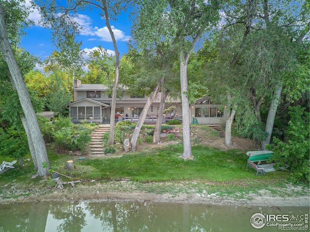 rear view of property featuring a sunroom, a yard, and a water view