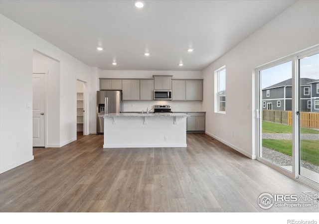 kitchen with gray cabinetry, stainless steel appliances, light hardwood / wood-style floors, a breakfast bar area, and a center island with sink