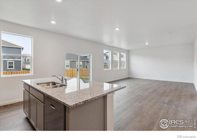 kitchen with light stone countertops, dishwasher, sink, light hardwood / wood-style flooring, and an island with sink