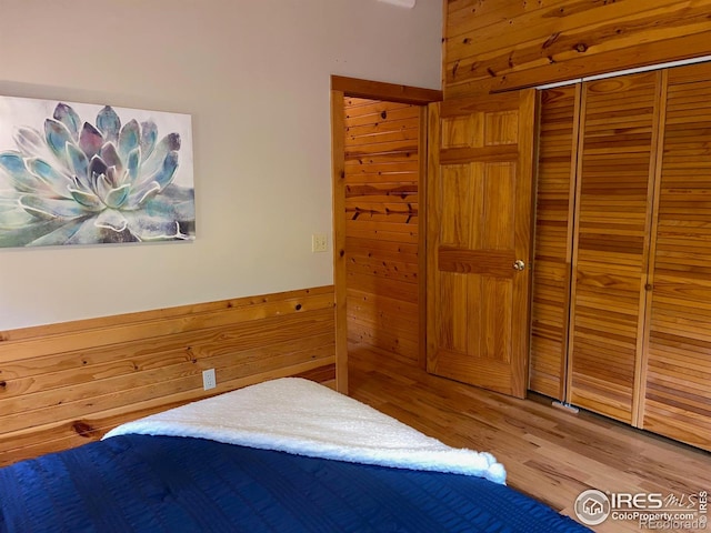 bedroom with wooden walls, a closet, and hardwood / wood-style floors