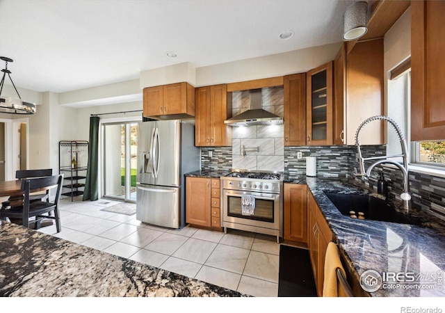 kitchen with wall chimney exhaust hood, light tile patterned flooring, stainless steel appliances, and dark stone counters