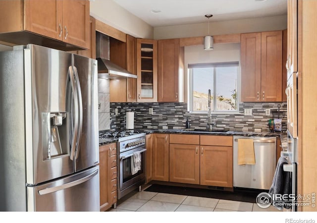 kitchen featuring dark stone counters, pendant lighting, sink, wall chimney exhaust hood, and appliances with stainless steel finishes