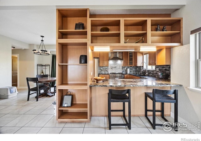 kitchen with pendant lighting, stone counters, a kitchen bar, kitchen peninsula, and wall chimney exhaust hood