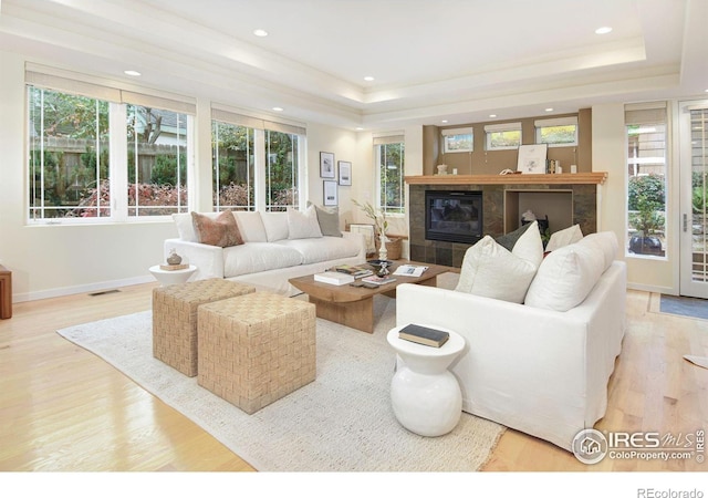 living room featuring a tray ceiling, light wood-type flooring, and a tile fireplace