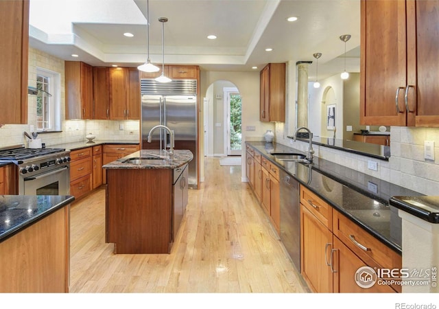 kitchen with dark stone countertops, premium appliances, a tray ceiling, and hanging light fixtures