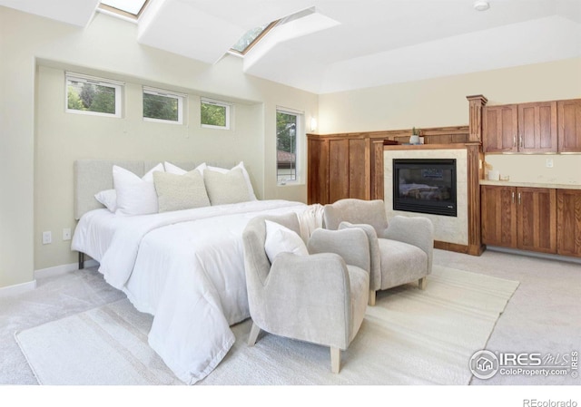 bedroom with multiple windows, a skylight, light colored carpet, and a fireplace