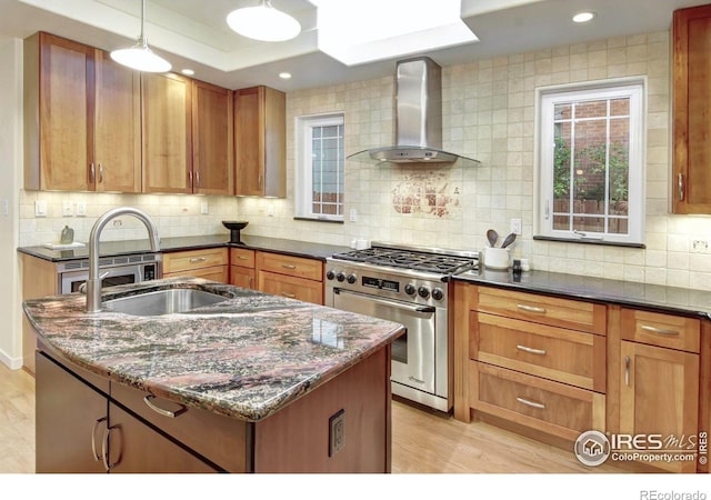 kitchen featuring wall chimney exhaust hood, backsplash, high end stainless steel range oven, dark stone counters, and light wood-type flooring