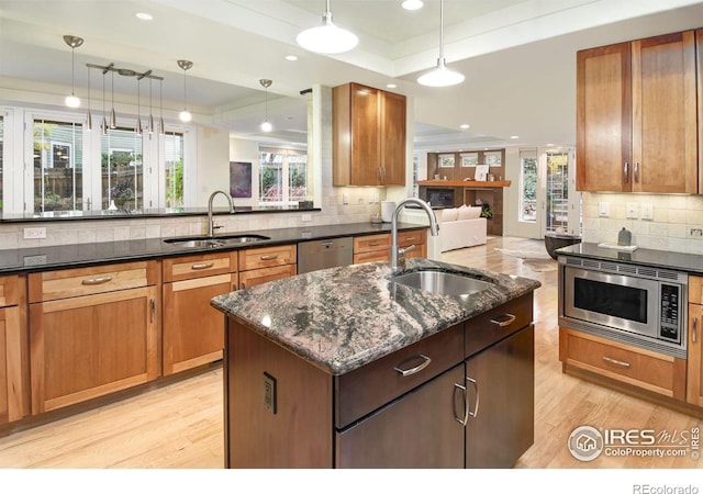 kitchen with a kitchen island with sink, stainless steel appliances, sink, pendant lighting, and a raised ceiling