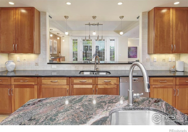 kitchen with dark stone countertops, tasteful backsplash, sink, and hanging light fixtures