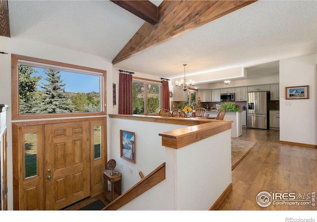 foyer featuring a textured ceiling, hardwood / wood-style floors, vaulted ceiling with beams, and a notable chandelier