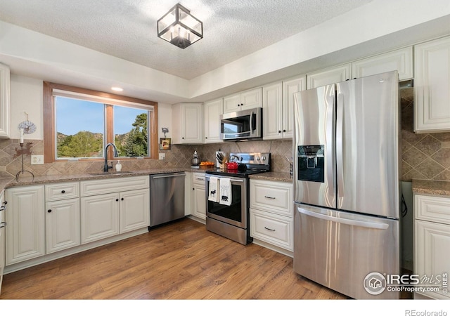 kitchen with light stone counters, appliances with stainless steel finishes, white cabinetry, and sink