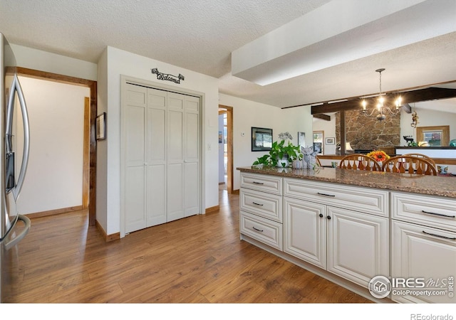 kitchen featuring stainless steel fridge with ice dispenser, light wood-type flooring, hanging light fixtures, white cabinets, and stone countertops