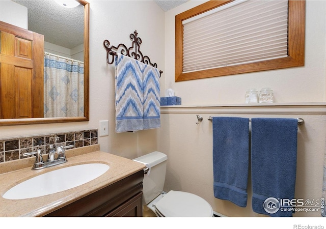 bathroom with a textured ceiling, backsplash, vanity, and toilet