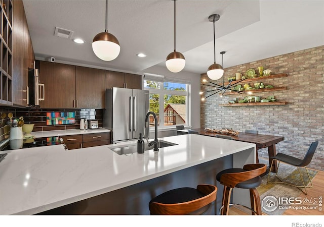 kitchen with dark brown cabinets, wood-type flooring, hanging light fixtures, stainless steel appliances, and sink