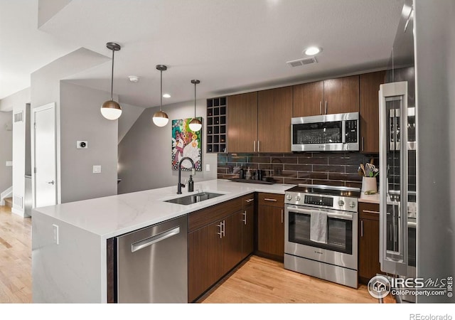 kitchen with appliances with stainless steel finishes, light hardwood / wood-style floors, kitchen peninsula, and sink