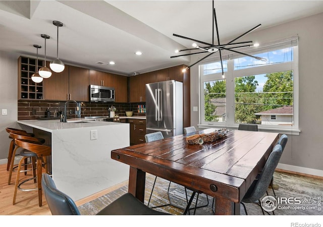 kitchen featuring light wood-type flooring, stainless steel appliances, kitchen peninsula, sink, and dark brown cabinetry