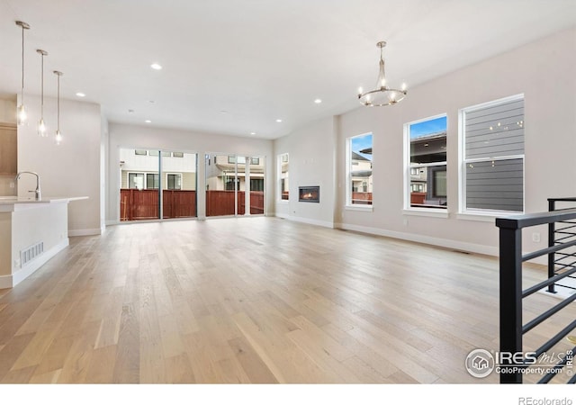 unfurnished living room with an inviting chandelier, a healthy amount of sunlight, sink, and light hardwood / wood-style flooring