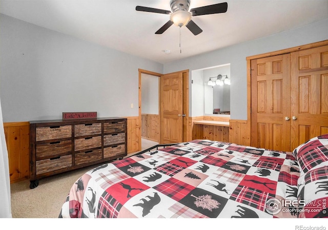 bedroom with wood walls, light carpet, ensuite bath, ceiling fan, and a closet