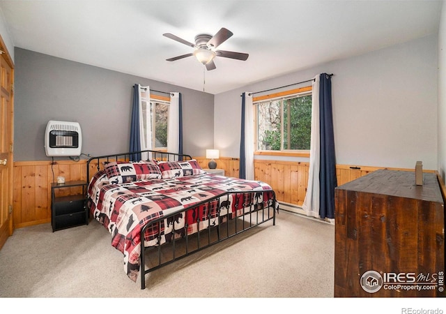 carpeted bedroom featuring heating unit, wooden walls, and ceiling fan