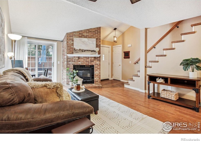 living room with a textured ceiling, vaulted ceiling, hardwood / wood-style floors, and a fireplace