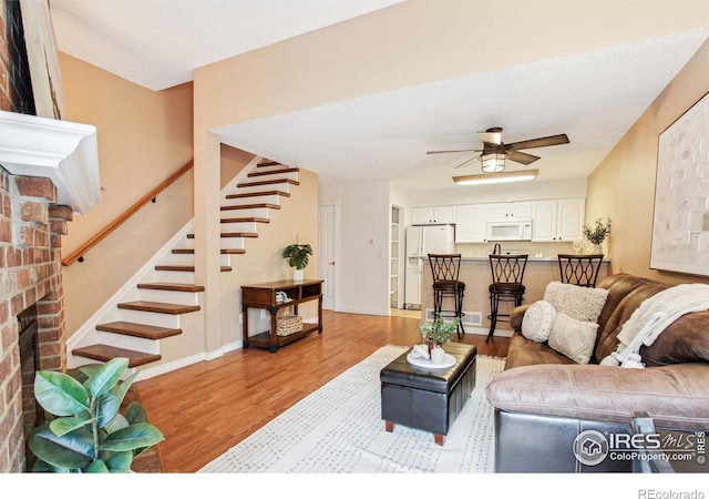 living room featuring a fireplace, a textured ceiling, light hardwood / wood-style flooring, and ceiling fan